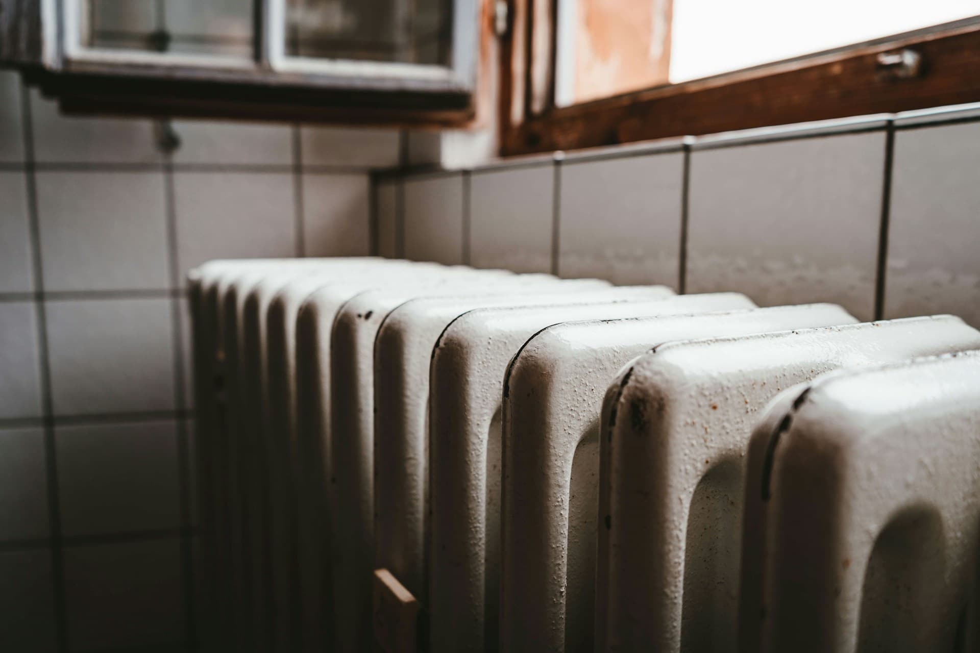 Biały grzejnik z głowicą termostatyczną pod drewnianą ramą okna